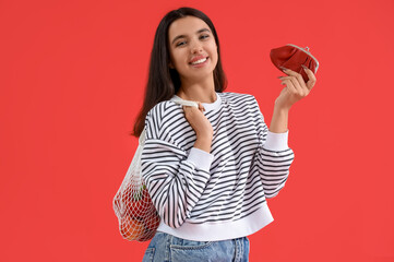 Poster - Young woman with wallet and string shopping bag on red background