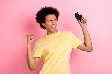 Poster - Portrait of delighted funky man hold controller closed eyes raise fist shout yes triumph isolated on pink color background