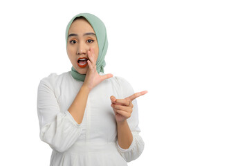 Wall Mural - Beautiful young Asian woman in green hijab and white blouse whispering to you and pointing finger at copy space isolated on white background