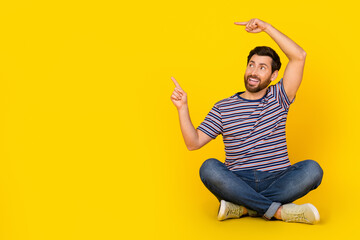 Sticker - Full body length photo of young guy in casual apparel sitting floor point fingers billboard isolated on yellow color background