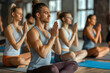 © MVProductions - Group of young people practicing yoga In the prayer position and raised hands while sitting on mat at gym, Concept of relaxation and meditation