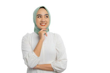 Wall Mural - Happy young Asian woman in green hijab and white blouse looking aside at empty space, touching chin, thinking of new good opportunities isolated on white background