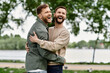© Bliss - Two bearded men hug each other while laughing in a green park.