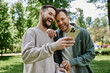 © Bliss - Two bearded gay men laugh together while looking at a smartphone in a green park.