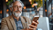 © Pavel Lysenko - An older man with a white beard smiles as he looks at his phone while sitting at a table in a cafe