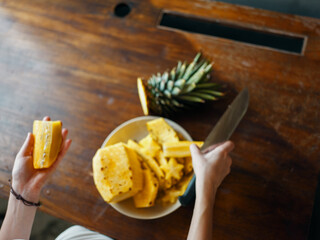Wall Mural - Person preparing to slice fresh pineapples on rustic wooden table with sharp knife