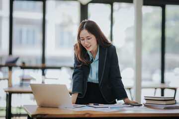 Wall Mural - Young Asian professional business woman office worker analyst sitting at desk working on laptop thinking on project plan, analyzing marketing or financial data online, watching elearning webinar.