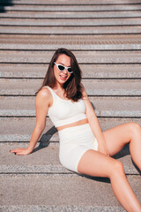 Wall Mural - Young beautiful smiling female in trendy summer white cycling shorts and tank top clothes. Sexy carefree woman posing in street. Positive model. Cheerful and happy.  Slim and fit body. In sunglasses