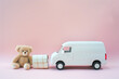 © Ostrich - Teddy bear with white toy delivery van on a pale pink background with copy space. Soft toy with truck and mail package.