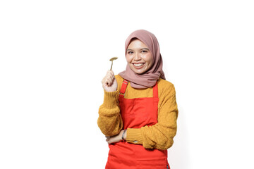 Wall Mural - Smilling young Asian Muslim woman wearing red apron holding spoon and fork isolated on white background