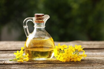 Wall Mural - Rapeseed oil in glass jug and beautiful yellow flowers on wooden table outdoors