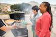 © DisobeyArt - Happy multiracial friends having fun cooking healthy food with barbecue at rooftop house outdoor - Multigenerational people grilling chicken during summer weekend meal - Focus on african woman ear