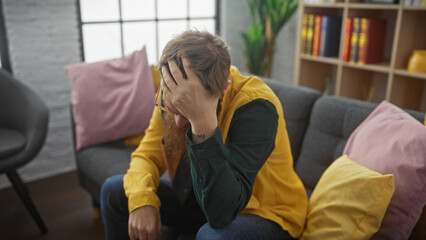 Sticker - Man in despair sitting on a sofa indoors, covering face with hands, showing stress, sadness or depression.