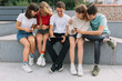 © anatoliycherkas - Group of teenagers sitting outdoors using their mobile phones.