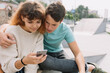 © anatoliycherkas - Two teenager, boy and girl in the park and using smartphone.
