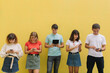 © anatoliycherkas - Group of teenagers using their mobile phones and tablet on a yellow background with copy space