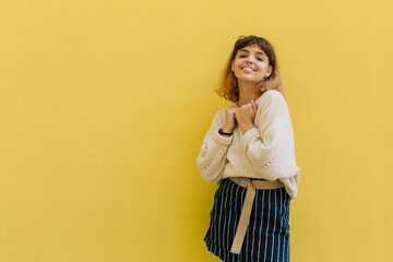 Smiling young teenage latinos girl with curly hair while standing alone against a yellow background