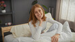 © Krakenimages.com - A smiling young caucasian woman lounges casually on a bed in a cozy bedroom setting, exuding a comfortable and homely vibe.