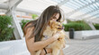 © Krakenimages.com - Beautiful young hispanic woman expressing love, hugging her pet dog, kissing it outdoors in a city park; an adult striking a portrait-style pose, standing amidst nature's green.