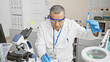 © Krakenimages.com - A middle-aged hispanic man in lab attire meticulously taking notes in a modern laboratory setting.