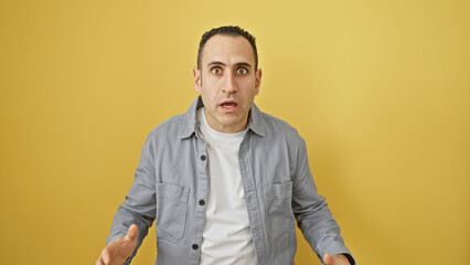 a shocked hispanic man in casual attire standing against a yellow isolated background, expresses sur