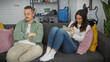 © Krakenimages.com - Upset man and engaged woman sitting separately on a couch in a modern living room, reflecting relationship issues.