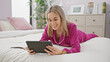 © Krakenimages.com - Smiling young caucasian woman in pink pajamas browsing tablet in her bedroom