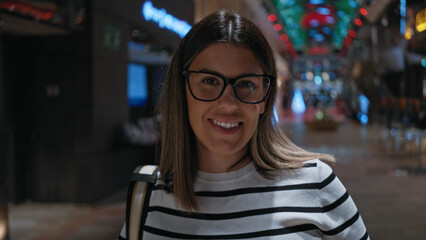 Wall Mural - Smiling brunette woman with glasses on a luxury cruise ship interior, illuminated by colorful lights.