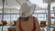 © Krakenimages.com - Rear view of a relaxed woman wearing a wide-brimmed hat, lounging by an upscale poolside with a sea backdrop.