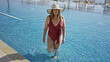 © Krakenimages.com - A young woman in a stylish swimsuit and sunhat walking through a sparkling pool at a luxury resort.