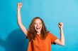 © deagreez - Photo of young successful red haired girl in orange t shirt raised fists up celebrating boyfriend winning isolated on blue color background