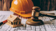 © Maksym - A legal gavel placed on architectural plans, accompanied by a construction helmet and a miniature house model, representing labor and construction law.