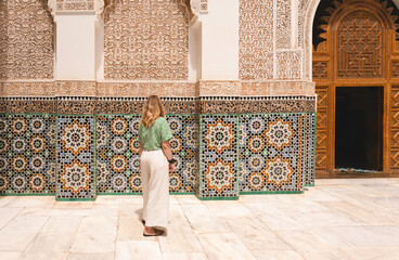 Casual young female woman solo traveler standing looking at beautiful traditional mosaic tile background, famous attraction, Ben Youssef, Marrakech, Morocco, cultural travel exploration vacation