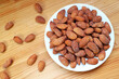 © jobi_pro - White Plate Full of Almonds with Some Kernels Scattered on Wooden Table