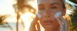 © narak0rn - Woman applying sunscreen to her face against the backdrop of a sunny, tropical setting for skin protection and care.