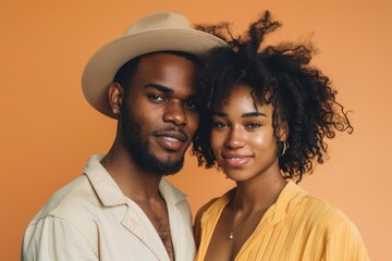 Wall Mural - Portrait of a blissful mixed race couple in their 20s donning a classic fedora on pastel orange background