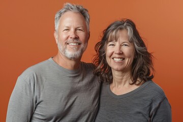 Wall Mural - Portrait of a smiling caucasian couple in their 40s sporting a long-sleeved thermal undershirt in front of pastel orange background