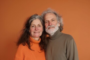 Wall Mural - Portrait of a merry couple in their 70s wearing a classic turtleneck sweater in front of pastel orange background