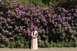 © Milou Dirks - classic picture of asian young woman in pink dress standing in front of large purple rhododendron flower  bush