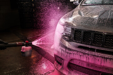 Wall Mural - Applying pink foam on the car by using the applicator. The process of cleaning car with pink foam. Manual vehicle washing at a self-service car wash.