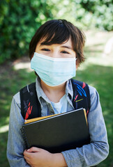 Boy, face mask and books for school in outdoor, confident and backpack for education. Male person, student and safety for virus or protect against germs, learning and child development at academy