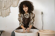 © sofiko14 - Young adult female potter using a pottery wheel to sculpt ceramic dishes in an art studio environment.
