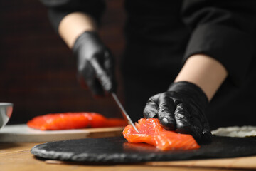 Wall Mural - Chef in gloves cutting salmon for sushi at table, closeup