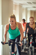 © ReadyAtTheEase/peopleimages.com - Woman, exercise bike and gym for spinning, training and cardio for fitness or cycling class. Female person, riding and stationary machine for workout challenge, aerobic instructor and equipment