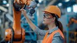 © nopommajun - A female engineer in protective gear works on programming an orange industrial robot arm in a manufacturing setting