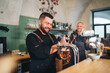 © Soloviova Liudmyla - Stylish bearded barman dressed black uniform smiling at camera, beer tapping at bar counter and waiter with tray. Successful people teamwork, friendship, brewing and restaurant industry concept image