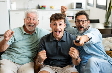Enthusiastic three generation men family fans watch football championship or olympic games on TV sitting together on sofa, happy grandson with father and old grandfather celebrate team victory