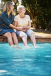 © ReadyAtTheEase/peopleimages.com - Mother, daughter and happiness by swimming pool for laughing, holding hands or relax in garden. Senior mom, woman and together in outdoor with smile for bonding, family or love and feet in water