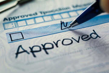 A close-up of an official document with a checkbox marked, signifying approval. The document might have a header like 