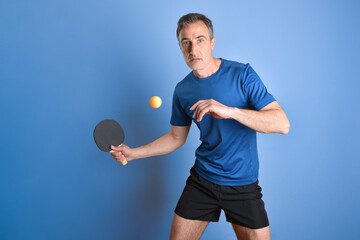 Wall Mural - Concentrated ping-pong player hitting a ball on blue isolated background